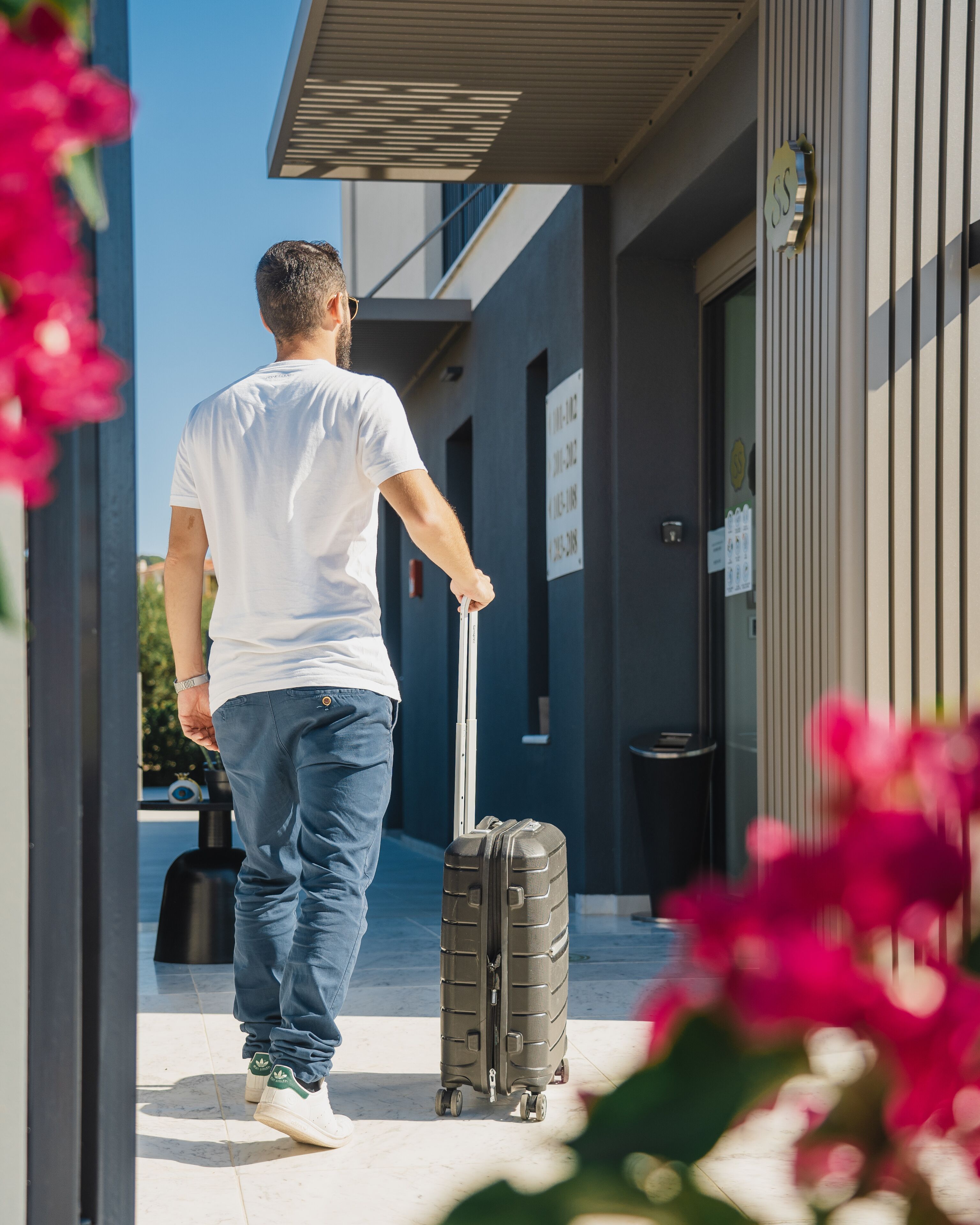 A man walking with a suitcase towards a building entrance.