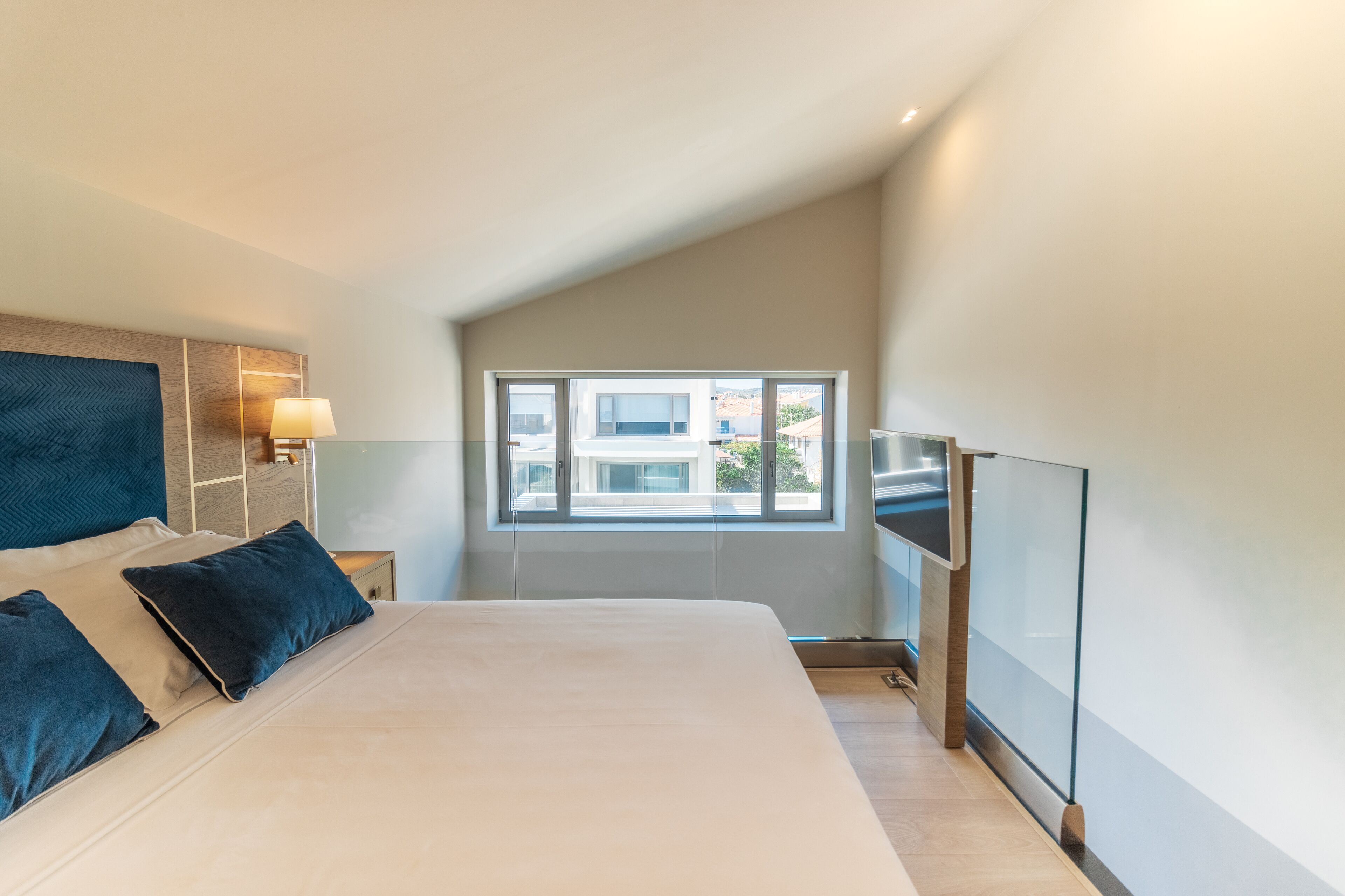 A modern bedroom with a large bed, a TV, and a window with a view of buildings.