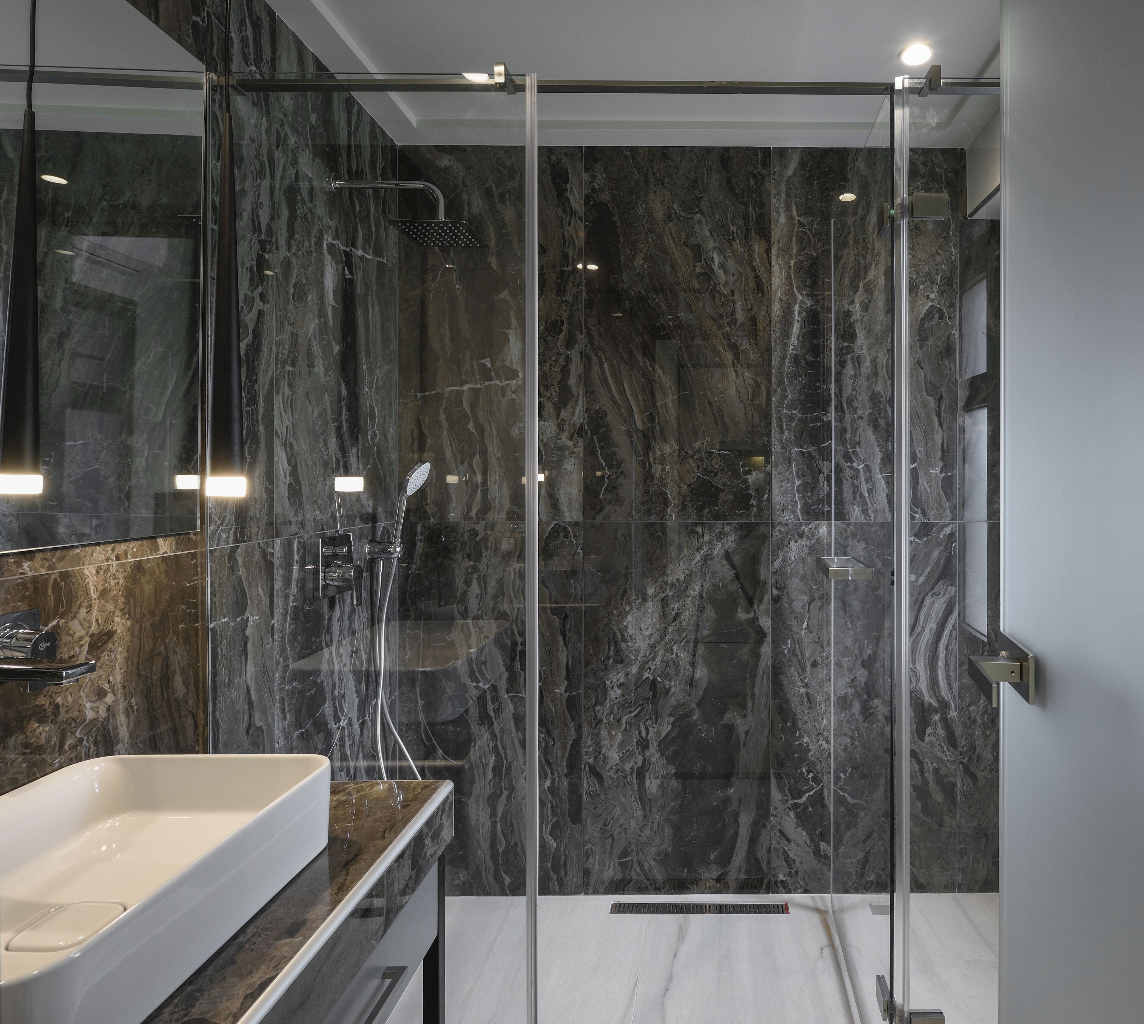 A modern bathroom with a glass-enclosed shower, a marble-tiled wall, and a white sink.