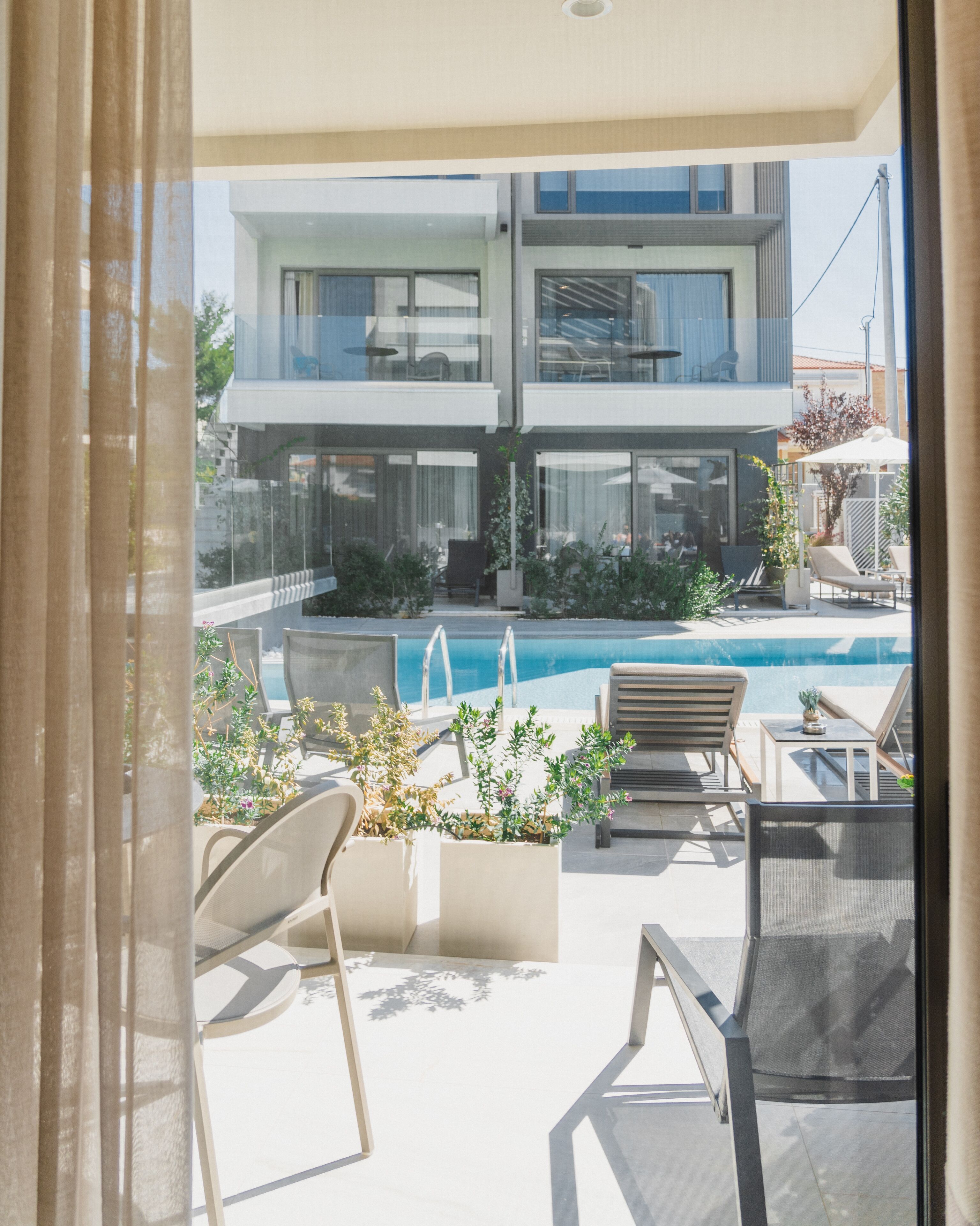 A modern outdoor pool area with lounge chairs and planters, overlooking a two-story building with large windows.