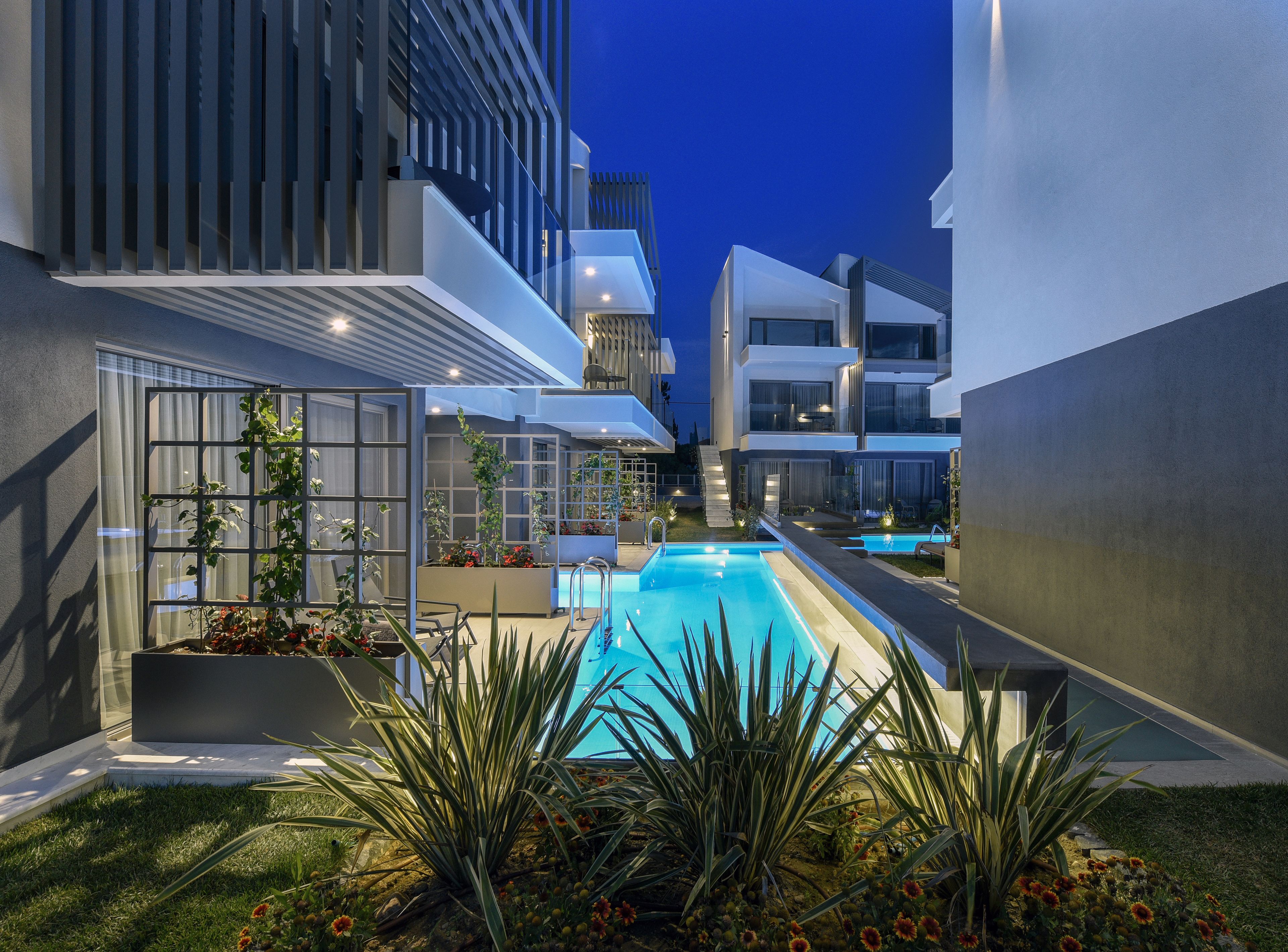 A modern pool area with a clear blue pool, surrounded by low-rise buildings and a well-maintained garden with various plants and flowers.