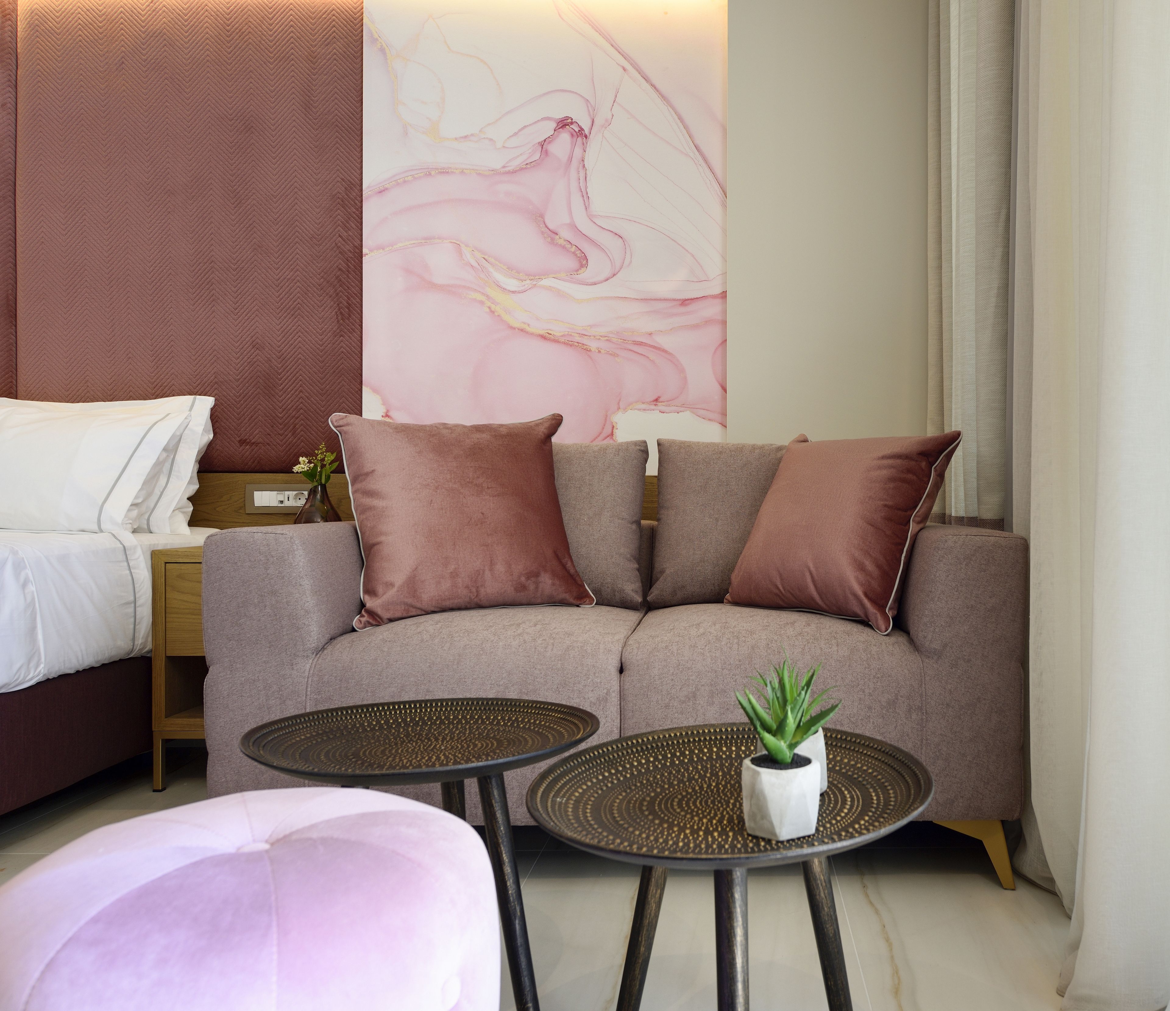 Et moderne hotelværelse med en sofa, to sofaborde, en lille potteplante og en dekorativ vægdekoration.