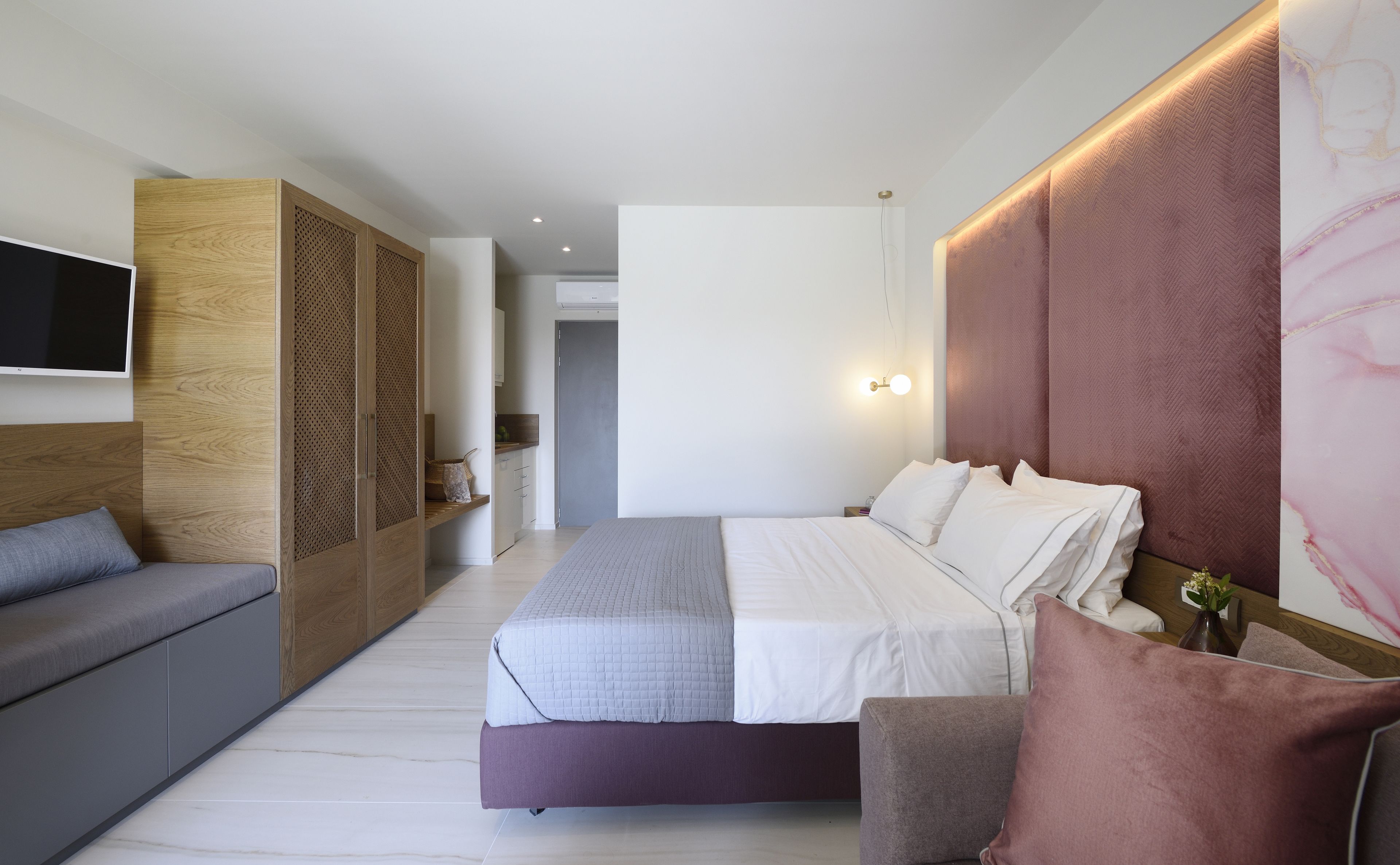 Un dormitorio moderno con una cama, un sofá, un televisor y una lámpara de pared.