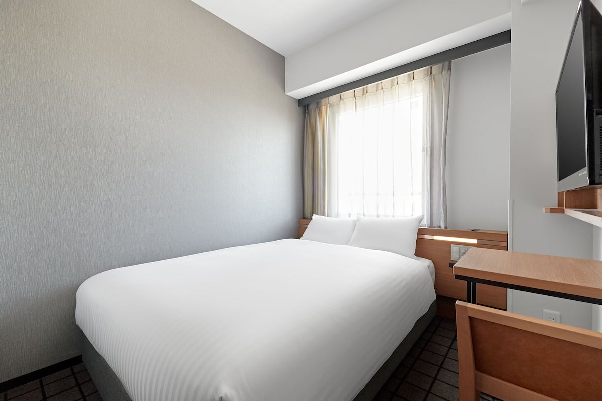 Une chambre d’hôtel avec un grand lit, un bureau, une télévision et une fenêtre avec des rideaux.