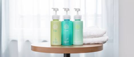 Three bottles of CUE body wash, shampoo, and conditioner on a wooden table with a white towel.