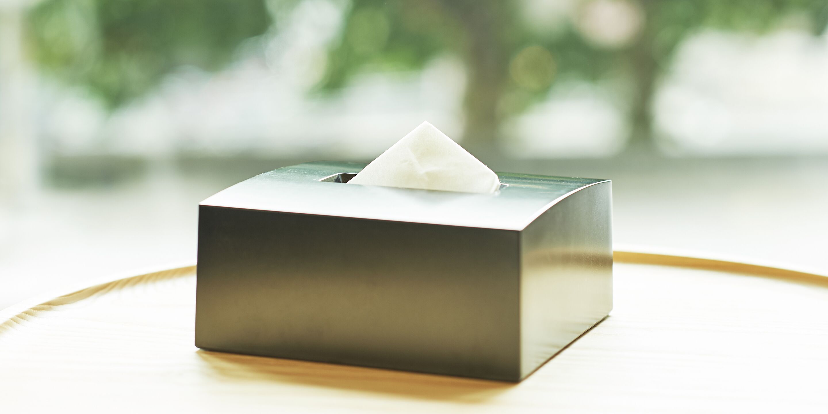 A tissue box on a wooden surface with a blurred green background.