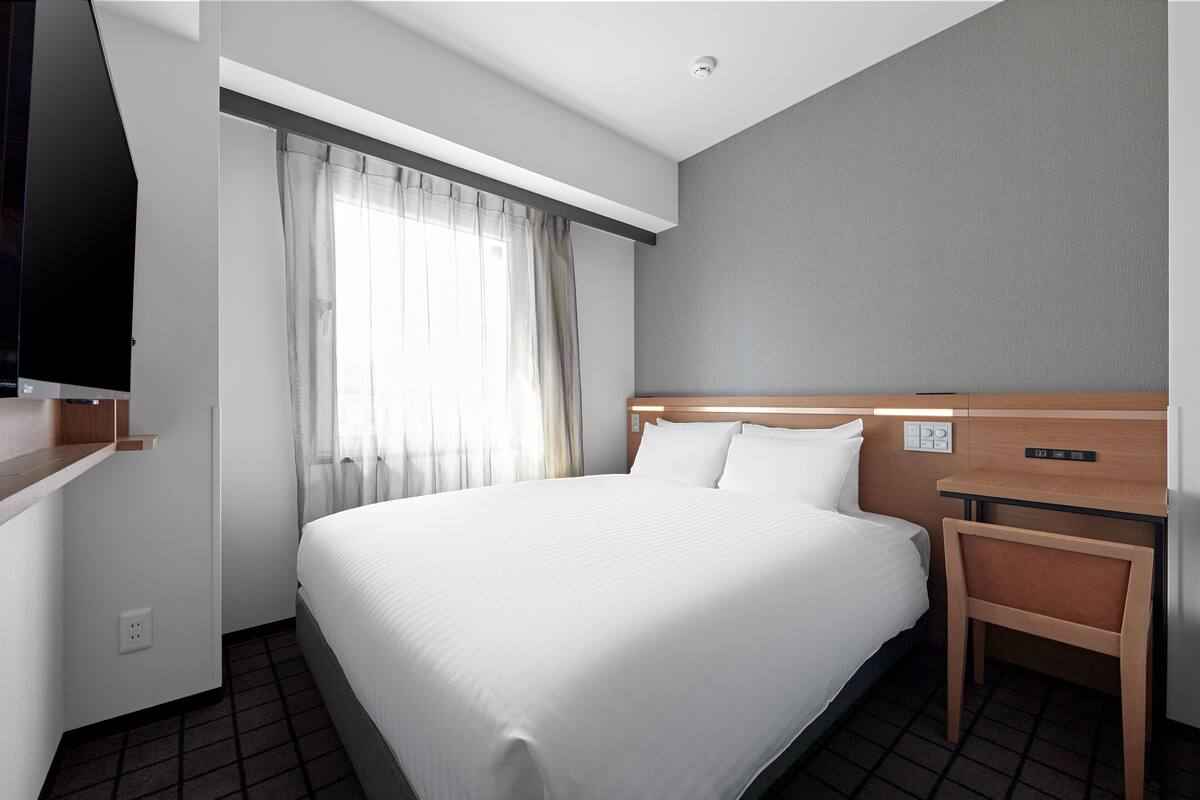 Une chambre d’hôtel avec un grand lit, une tête de lit en bois, une table de chevet, un téléviseur fixé au mur et une fenêtre avec des rideaux.