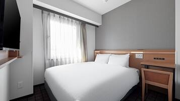 Una camera d'albergo con un letto grande, una testiera in legno, un comodino, una TV fissata al muro e una finestra con tende.