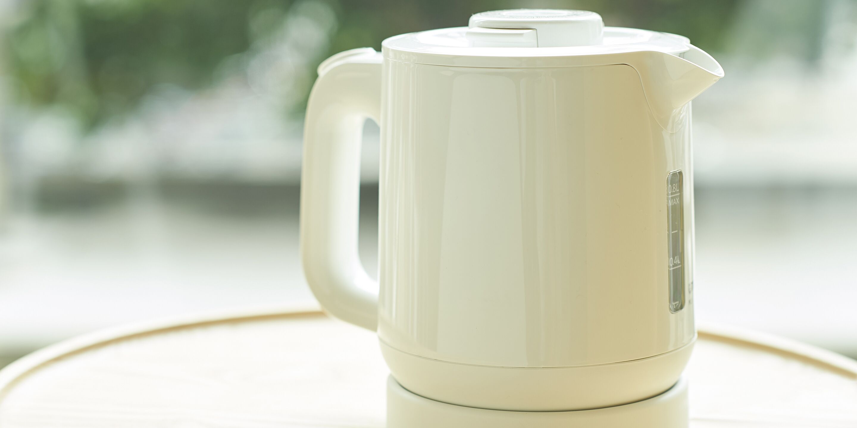 A white electric kettle with a handle and a spout, placed on a reflective surface.