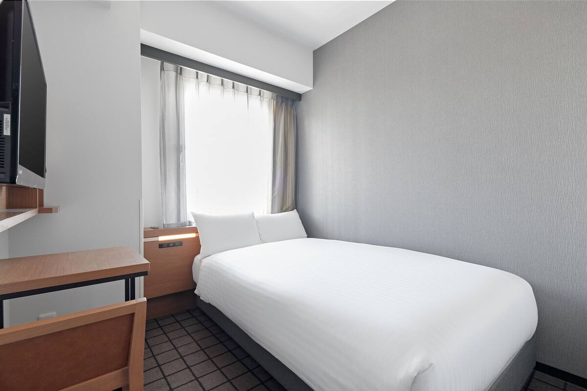 Une chambre d’hôtel équipée d’un lit, d’un bureau, d’une chaise, d’une fenêtre avec des rideaux et d’un téléviseur.