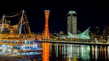A waterfront cityscape with illuminated buildings, a prominent tower, and a boat docked near the shore.