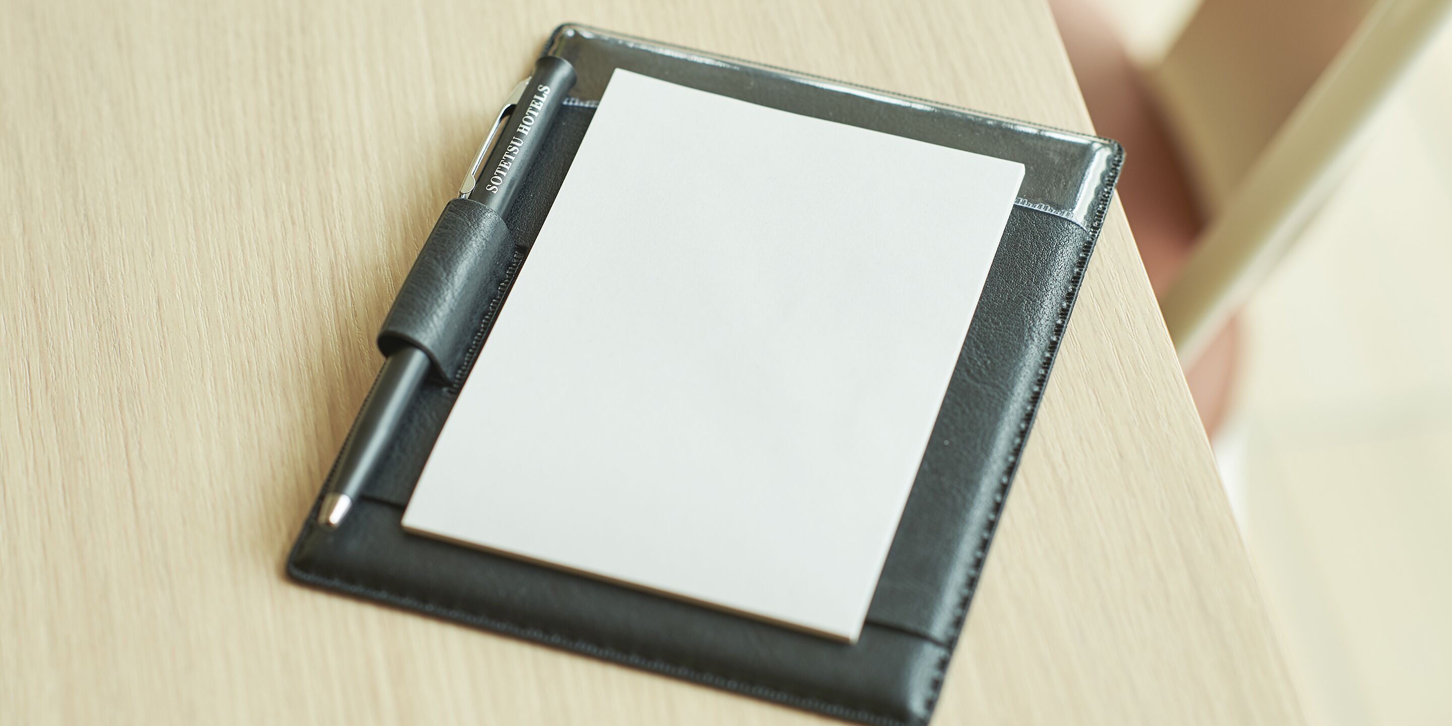 A black leather notebook with a white sheet of paper on a wooden surface.