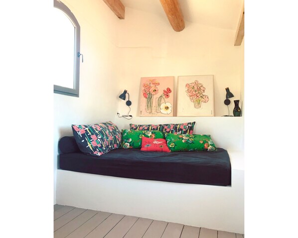 Une pièce chaleureuse avec un canapé noir, des coussins colorés et deux œuvres d’art florales encadrées accrochées au mur.
