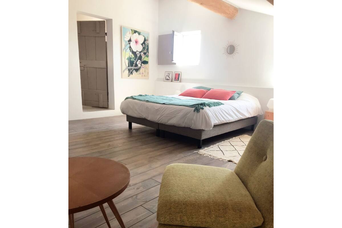 A bedroom with a bed, a chair, a table, and a painting on the wall.