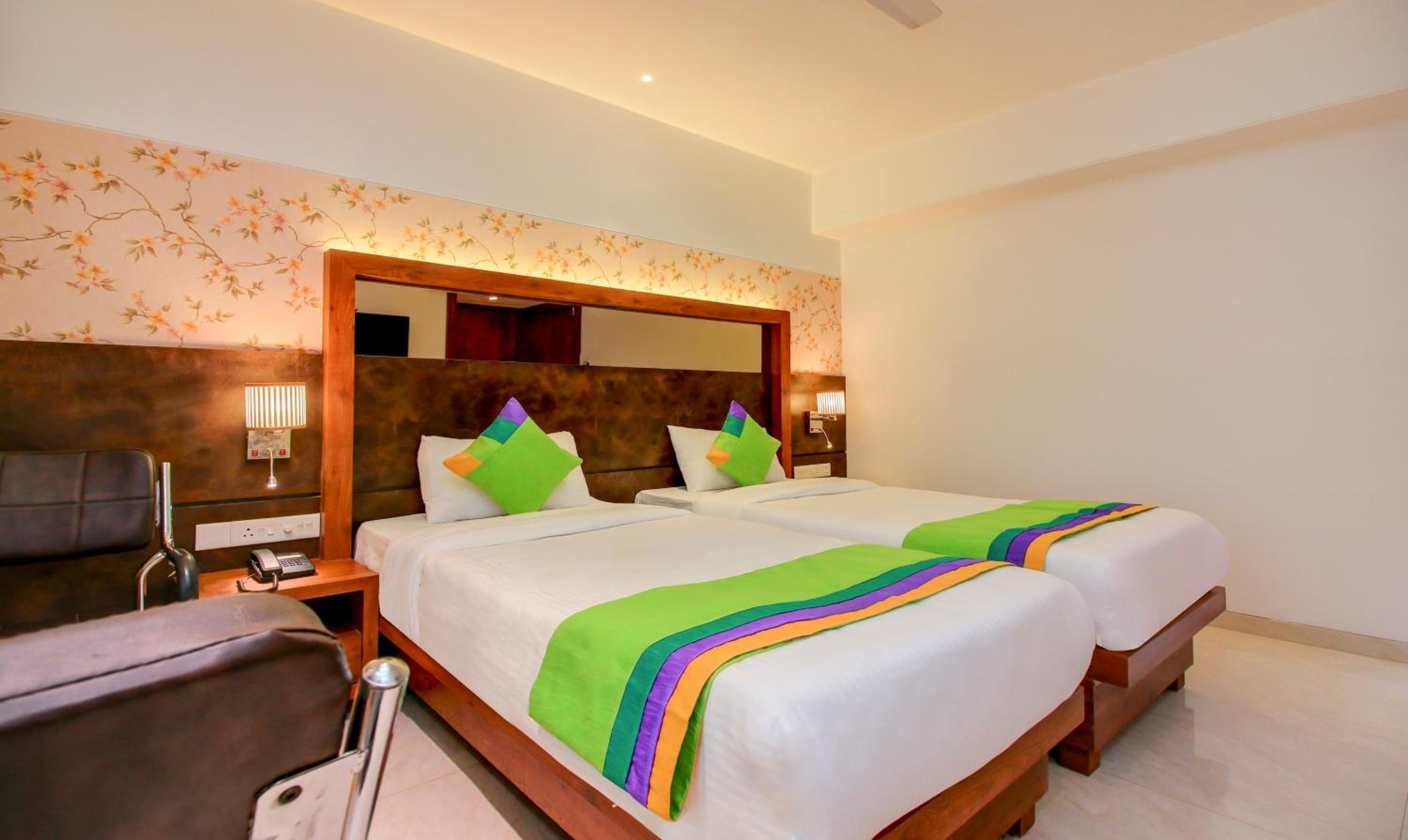 Habitación de hotel con dos camas, cabecera de madera, mesita de noche con lámpara y una silla.