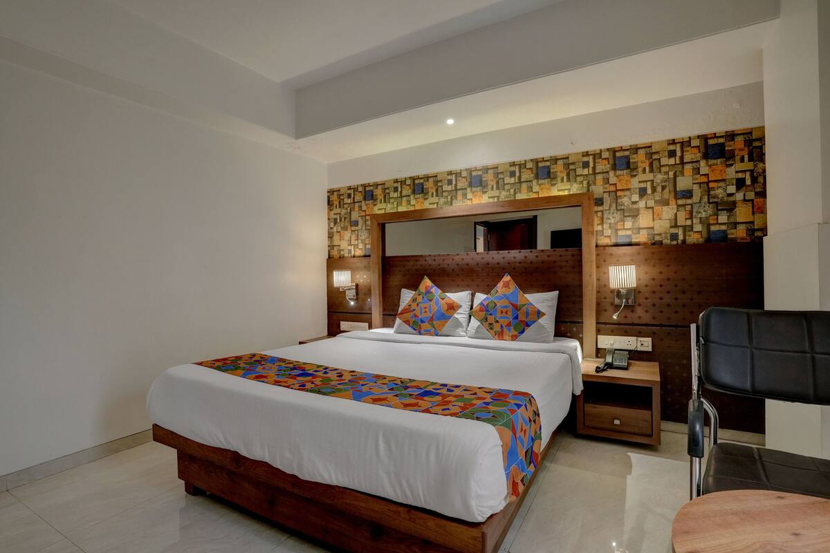 A neatly made bed with a patterned bedspread, a wooden headboard with a mosaic design, and a bedside table with a lamp and phone.