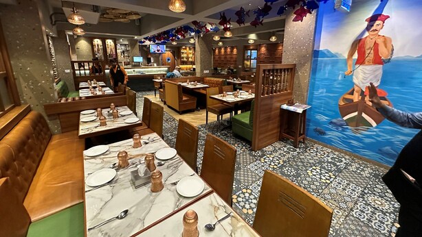Interior de un restaurante con cabinas, mesas y un mural de un hombre en un bote.