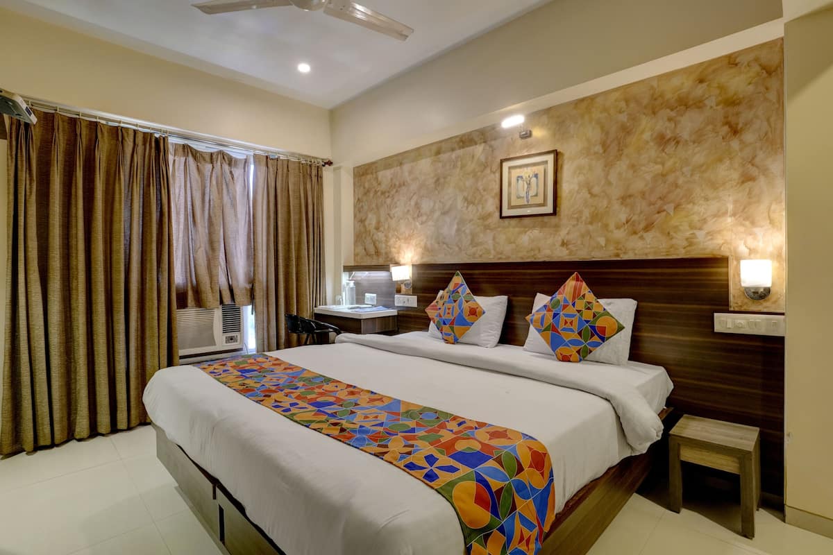 A hotel room with a bed, curtains, a headboard, bedside tables, and a wall-mounted light fixture.