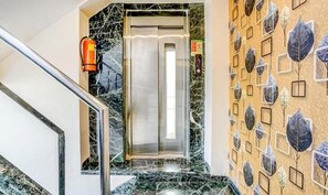 A marble staircase leading to an elevator, a fire extinguisher mounted on the wall, and a patterned wall with leaf designs. - Hotel SriKrishna Paradise Thane Airoli (Thane)