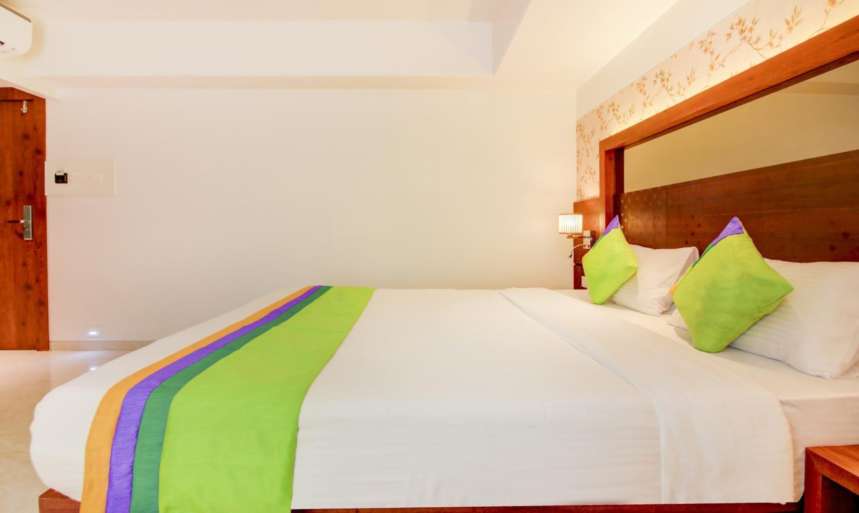 Una camera d'albergo con un letto grande, una testiera in legno e un comodino con una lampada.