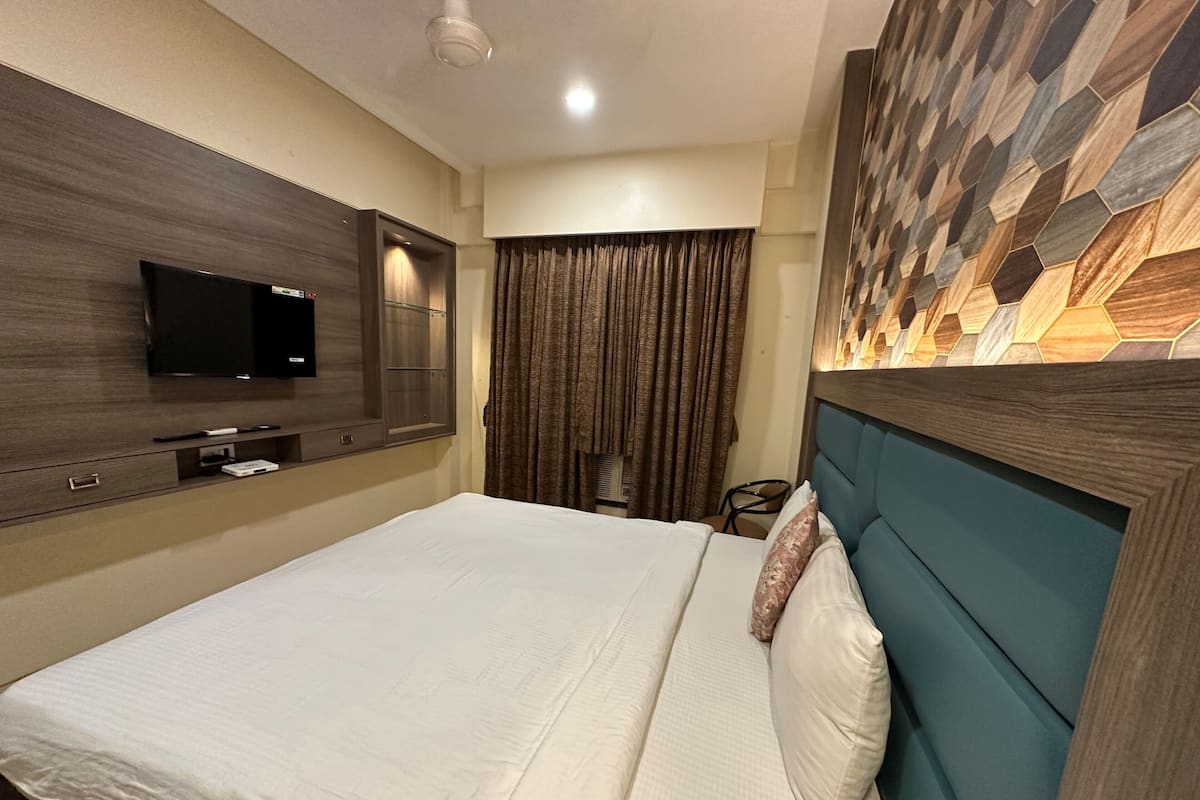 A hotel room with a bed, a television mounted on the wall, a desk with a chair, and a decorative wall panel.