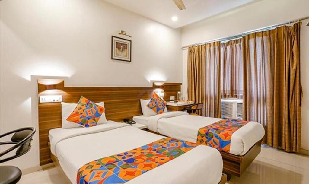 Una habitación de hotel con dos camas, un escritorio, una silla y una ventana con cortinas.