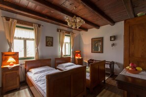 A bedroom with two wooden beds, a wooden wardrobe, a desk with a fruit bowl, and a chandelier.