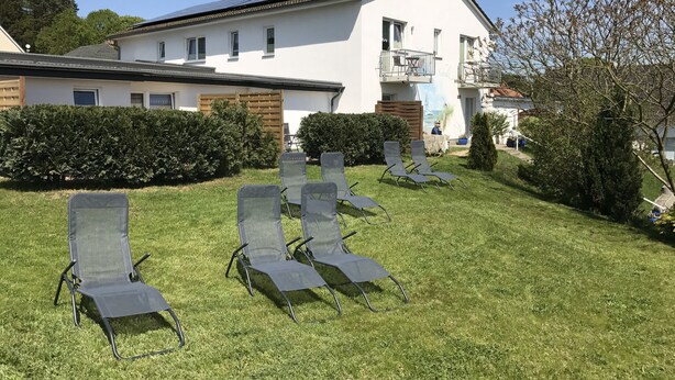 Ein Gebäude mit weißer Fassade, einem Balkon und einer Rasenfläche mit mehreren Liegestühlen.