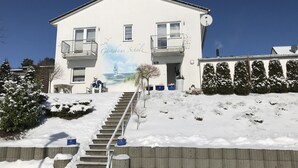 Ein zweistöckiges Gebäude mit einem Balkon im zweiten Stock, einem Wandgemälde eines Segelboots und einem Schild mit der Aufschrift 'Gästehaus Schul'.