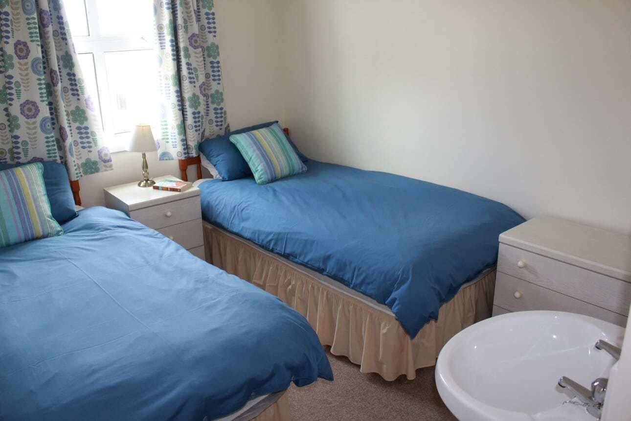 A bedroom with two beds, a bedside table with a lamp, a nightstand, and a bathroom with a sink and mirror.