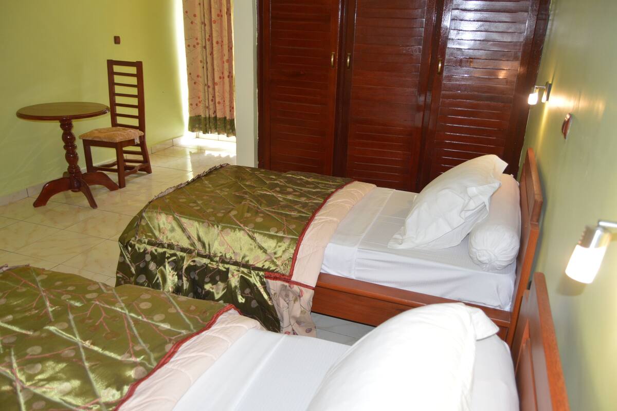 Una habitación con dos camas, una silla de madera, una mesita redonda pequeña y un armario de madera.