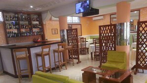 A bar area with a television mounted above the bar, wooden chairs, and a green sofa in the seating area. - Hôtel - Y (Douala)