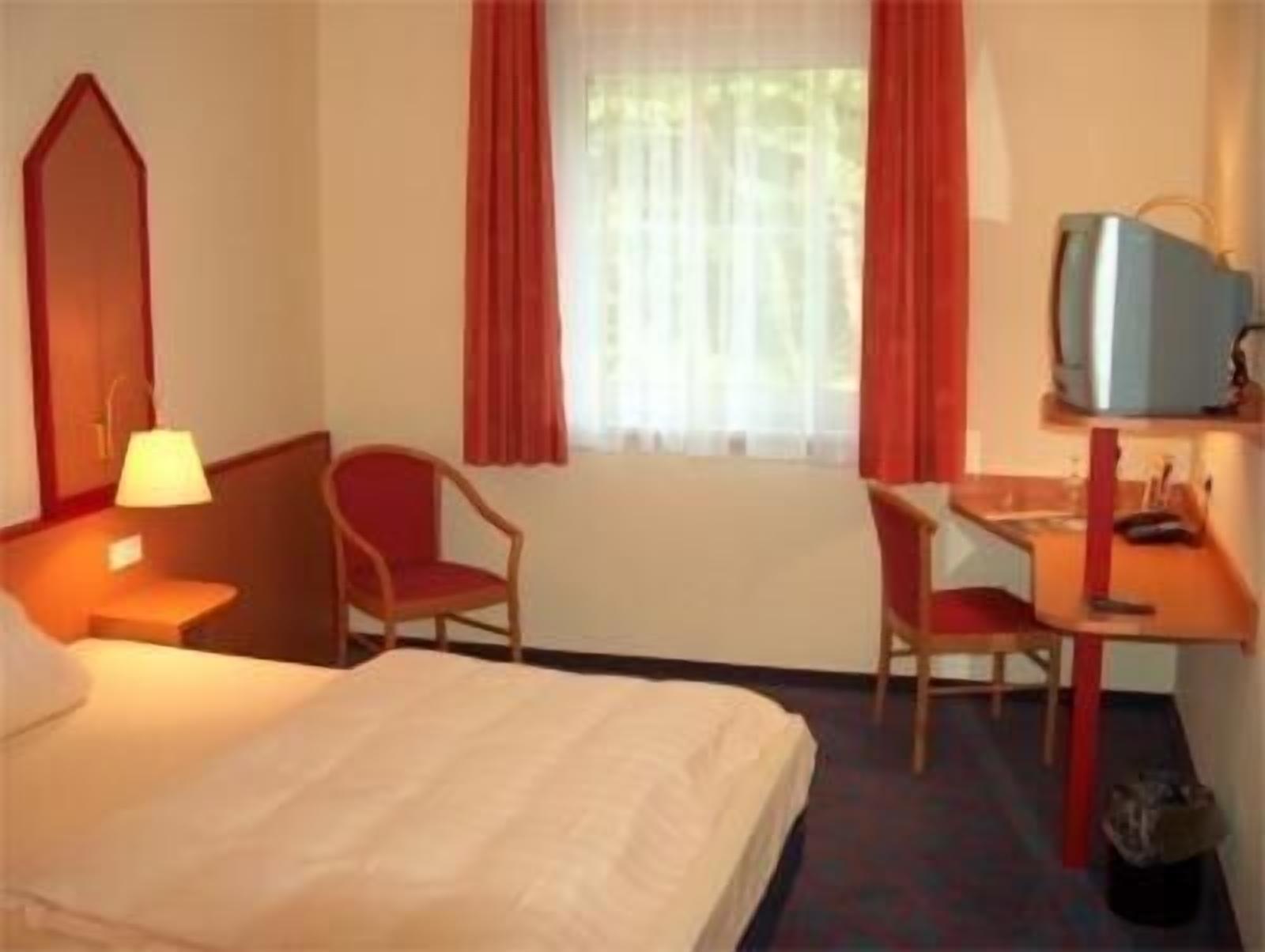 Hotellihuone, jossa on sänky, työpöytä, tuoli, televisio ja ikkuna, jossa on verhot.