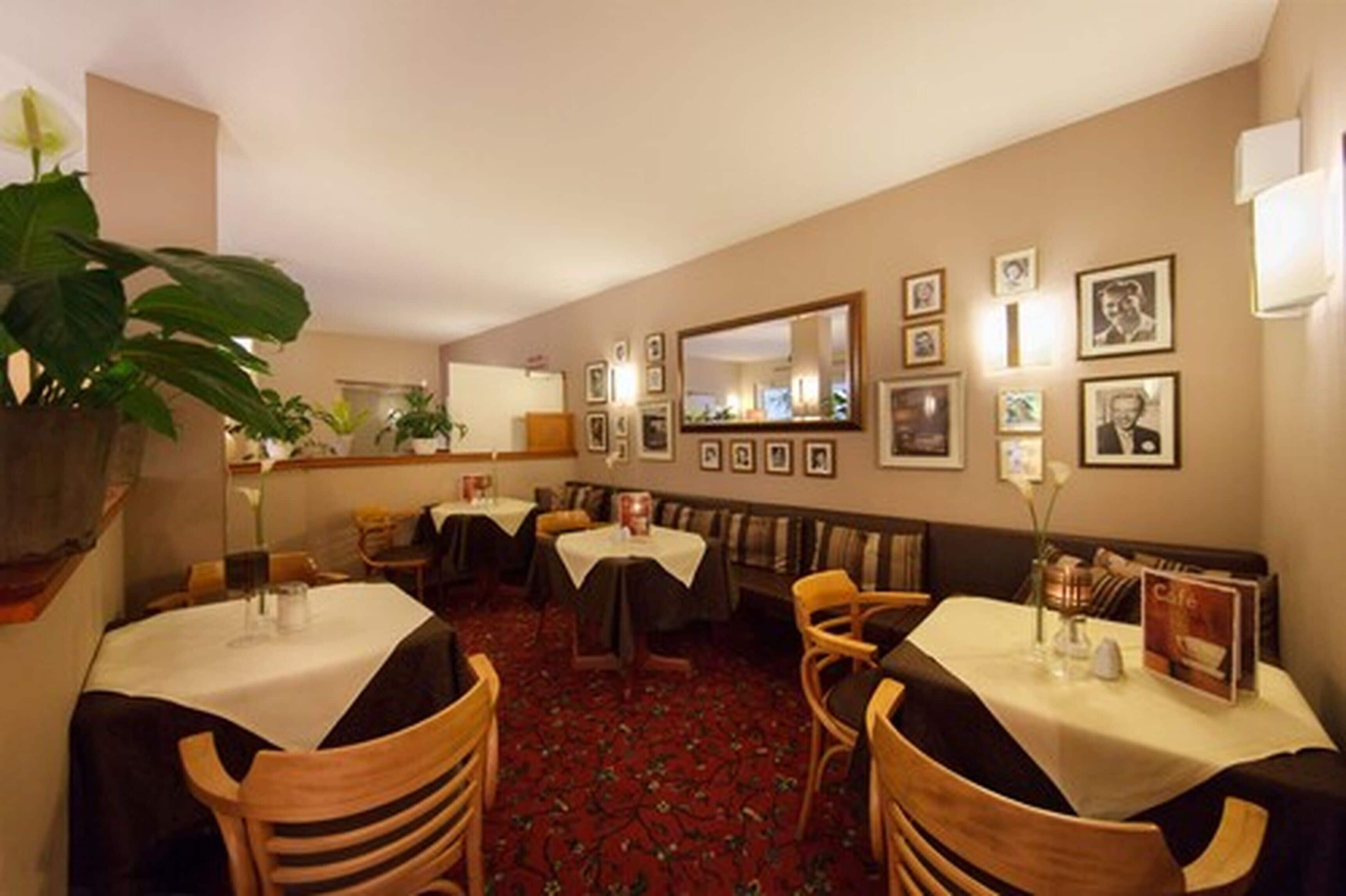 En restaurant med borde dækket af hvide duge, træstole og et rødt tæppe på gulvet.