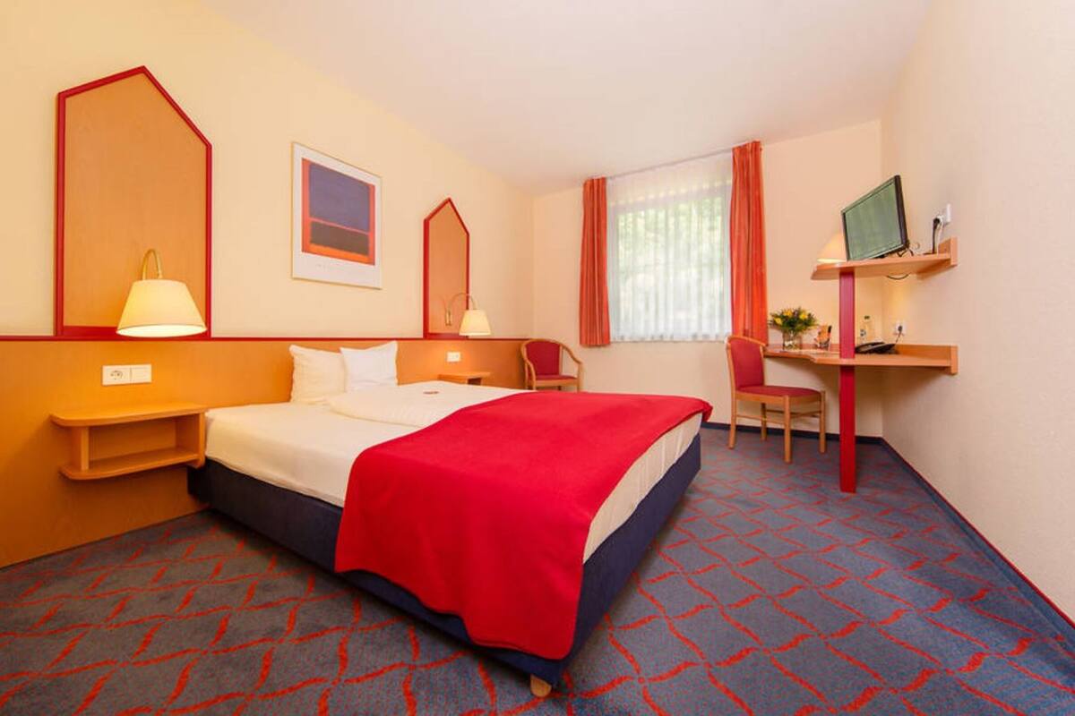 Een hotelkamer met een bed, een bureau, een stoel, een televisie en een raam met gordijnen.