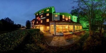 Un hotel con fachada curva, ventanas amplias y un espacio exterior bien iluminado con mesas y sillas.