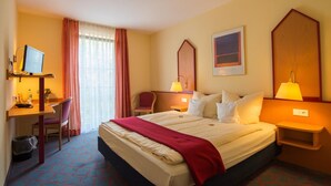 A hotel room with a bed, desk, chair, and two bedside lamps. - Montana Senden Münster (Senden)