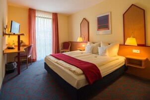 Habitación de hotel con cama, escritorio, silla y dos lámparas de noche.