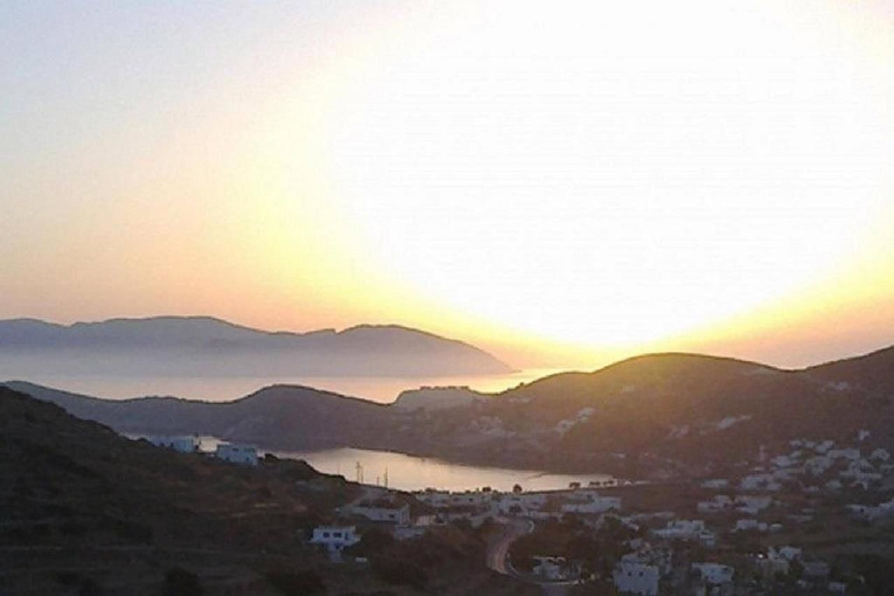 Un paysage côtier avec un lever ou un coucher de soleil, des collines, une étendue d’eau et un petit village avec des bâtiments.