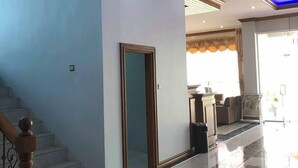 Un pasillo amplio con piso de mármol, una escalera con barandillas de madera y un techo moderno con iluminación empotrada.
