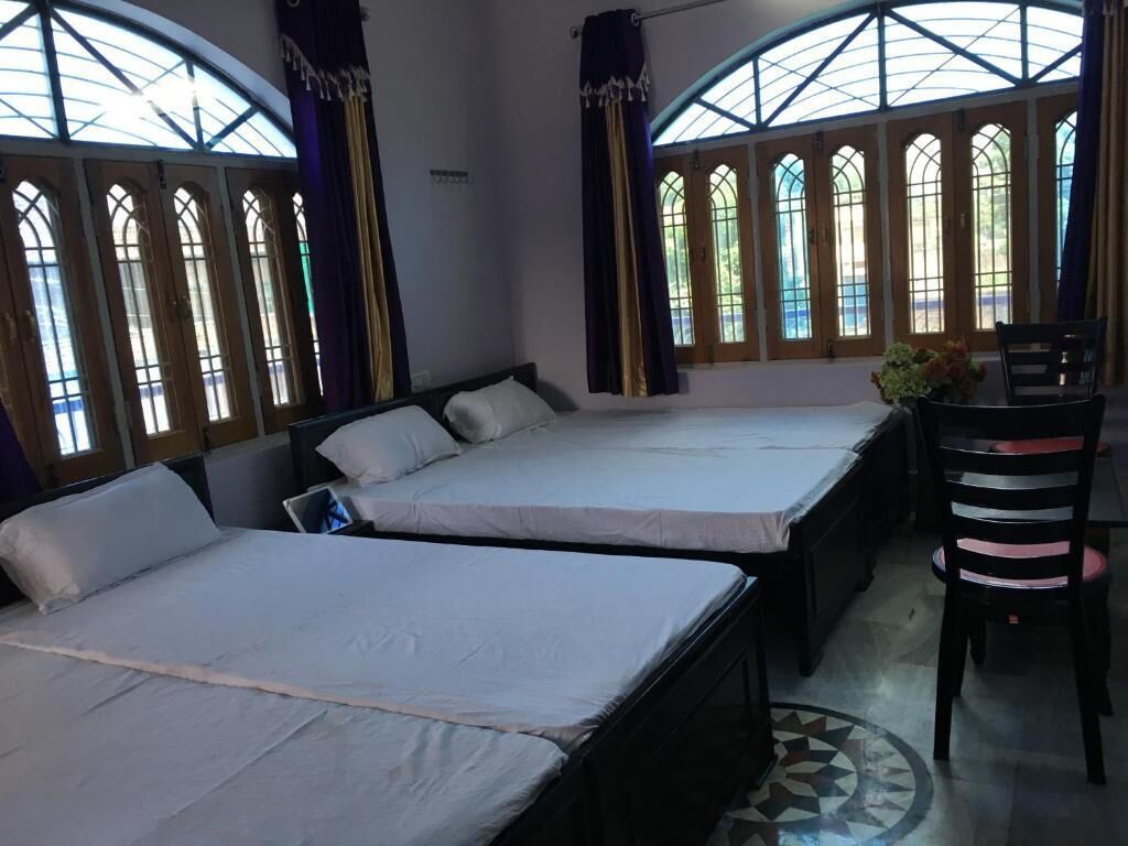 Quarto com duas camas, uma cadeira e grandes janelas com arcos.