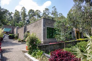 A modern building with a stone facade, large windows, and a paved pathway leading to it. - Musanze Caves Hotel (Muhoza)