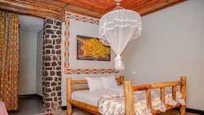 Uma cama de madeira rústica com um cobreleiro branco, parede de pedra, tapete colorido e mosquiteiro pendurado.