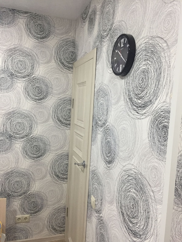 Simple, functional room with a distinctive wallpaper pattern and a clock for keeping time.
