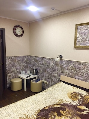 Relax in a stylish room with a floral-patterned bedspread, a small table, and a clock on the wall.