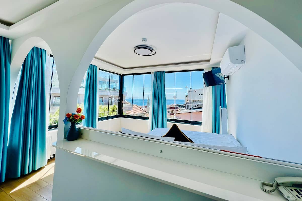 A modern hotel room with a large arched window, a bed, a bedside table, and a telephone.