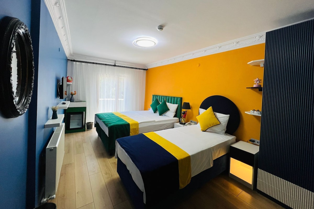 A hotel room with two beds, a desk, a chair, a mirror, and a window with curtains.