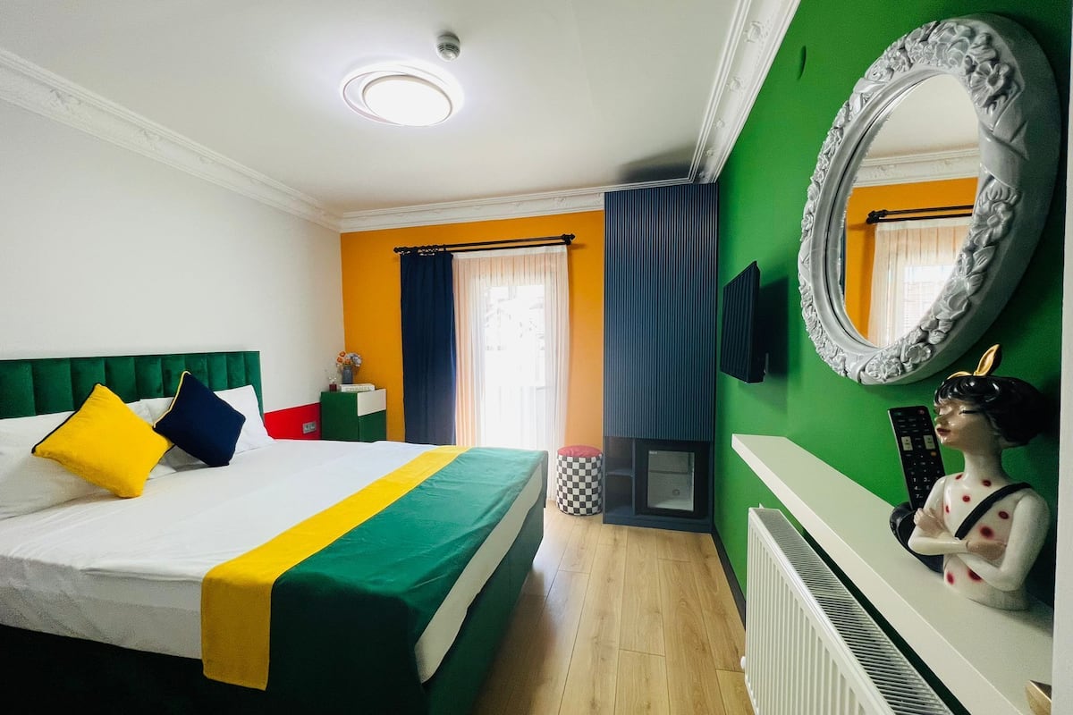 A hotel room with a bed, a green wall, a large mirror, and a statue.