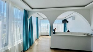 A hotel room with a wooden floor, a reception desk, and a large window with blue curtains. - Apex Hotel (Istanbul)