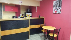 A small cafe with a red wall, a wooden counter, and a table with chairs. - Hôtel La Brise (Ain El Turk)